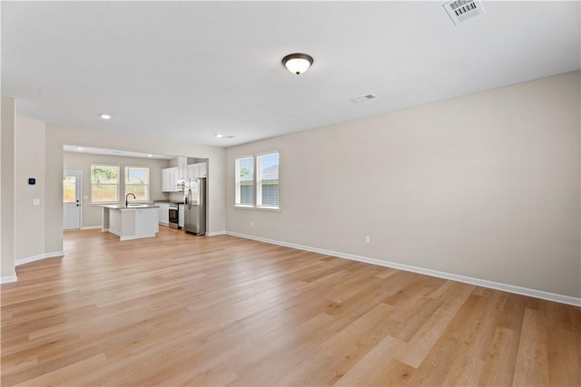 unfurnished living room featuring a sink, baseboards, light wood-style floors, and visible vents