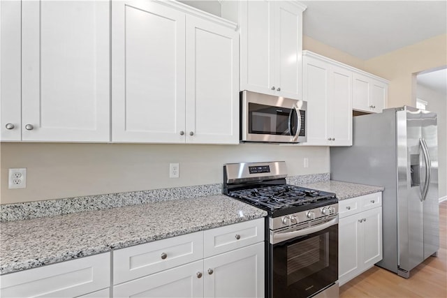 kitchen with white cabinets, light stone countertops, appliances with stainless steel finishes, and light wood-style flooring
