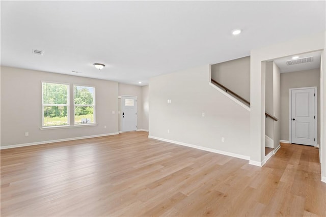unfurnished living room with baseboards, light wood finished floors, stairs, and visible vents