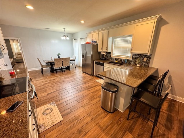 kitchen with hanging light fixtures, light hardwood / wood-style flooring, kitchen peninsula, stainless steel appliances, and backsplash