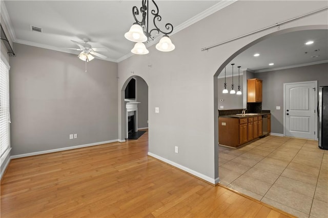 unfurnished dining area featuring sink, light wood-type flooring, ceiling fan with notable chandelier, and ornamental molding