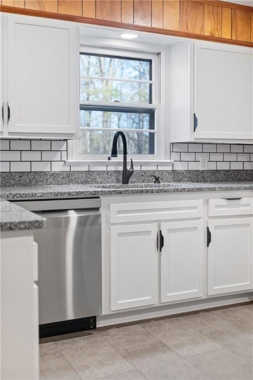 kitchen with light tile patterned floors, decorative backsplash, stainless steel dishwasher, white cabinetry, and light stone countertops