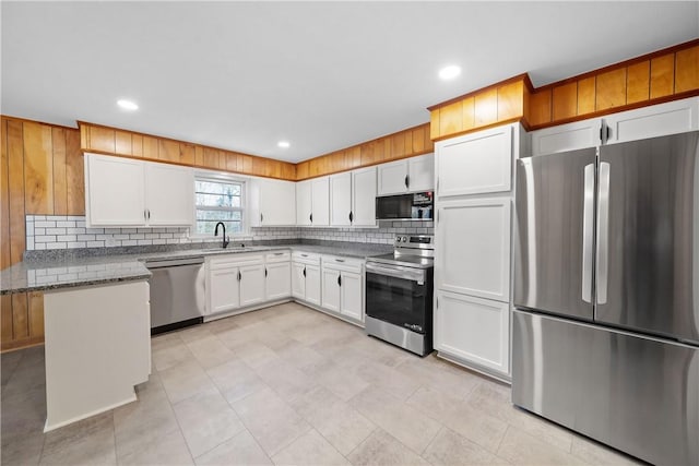 kitchen featuring light stone counters, stainless steel appliances, decorative backsplash, white cabinets, and a sink