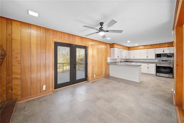 kitchen with french doors, stainless steel electric range oven, wood walls, built in microwave, and a peninsula