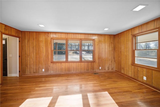 unfurnished room featuring light wood-style floors, wood walls, and baseboards