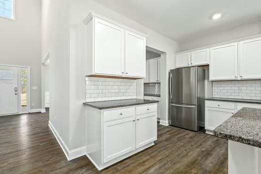 kitchen featuring baseboards, white cabinets, dark wood finished floors, dark stone countertops, and freestanding refrigerator