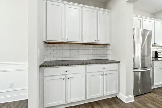 kitchen featuring dark wood-type flooring, backsplash, freestanding refrigerator, and white cabinetry