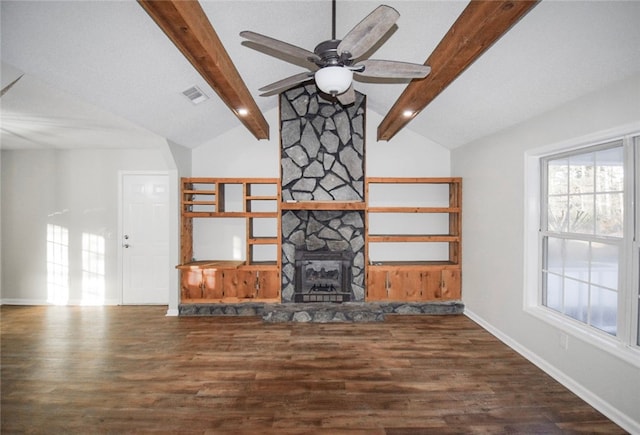 unfurnished living room featuring dark hardwood / wood-style flooring, ceiling fan, a stone fireplace, and lofted ceiling with beams