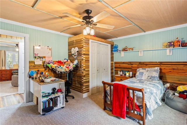 carpeted bedroom with a closet, ceiling fan, and wooden walls