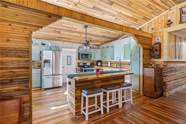 kitchen with wooden walls, hardwood / wood-style floors, appliances with stainless steel finishes, and vaulted ceiling