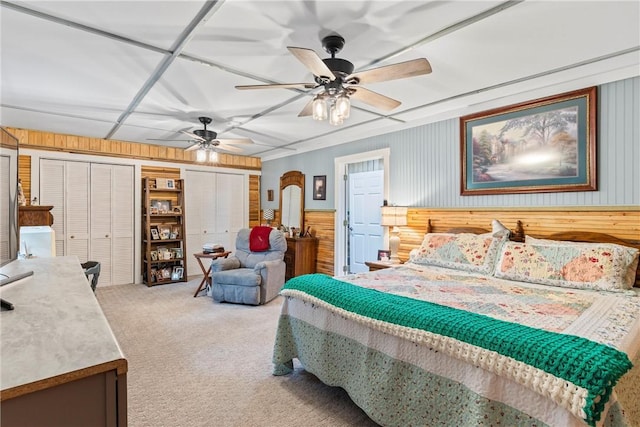 carpeted bedroom featuring ceiling fan, multiple closets, and wood walls