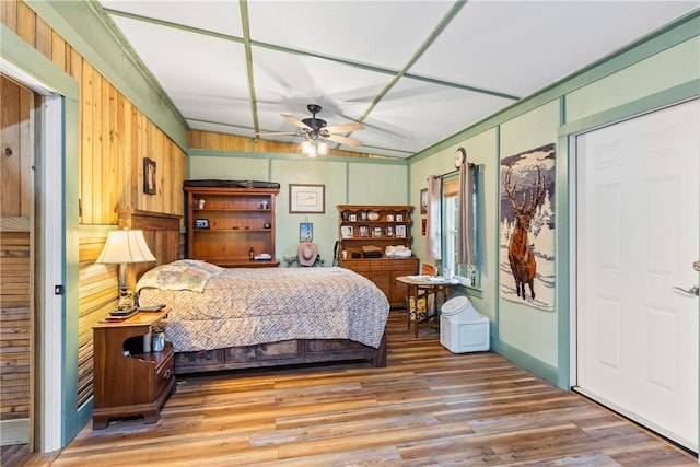 bedroom featuring ceiling fan, crown molding, wood-type flooring, and wooden walls