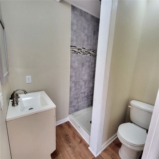 bathroom with hardwood / wood-style flooring, vanity, toilet, and a tile shower