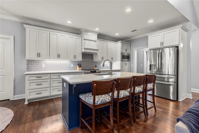 kitchen with white cabinets, appliances with stainless steel finishes, sink, a kitchen island with sink, and a breakfast bar area