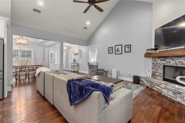 living room with high vaulted ceiling, dark hardwood / wood-style floors, a stone fireplace, and ceiling fan with notable chandelier