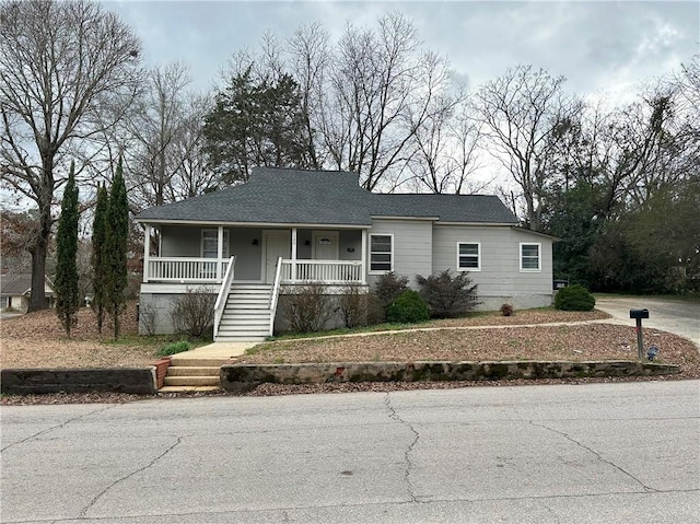 view of front of house with a shingled roof, a porch, and stairway