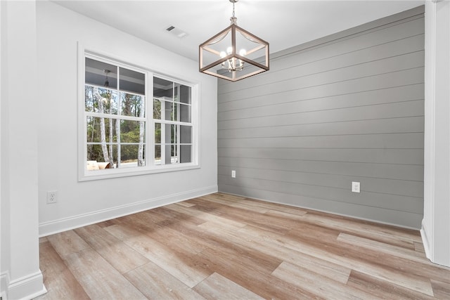 unfurnished dining area featuring light hardwood / wood-style flooring, an inviting chandelier, and wood walls