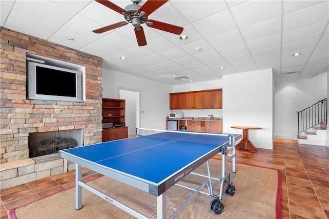 recreation room featuring a stone fireplace, sink, a drop ceiling, and tile patterned floors