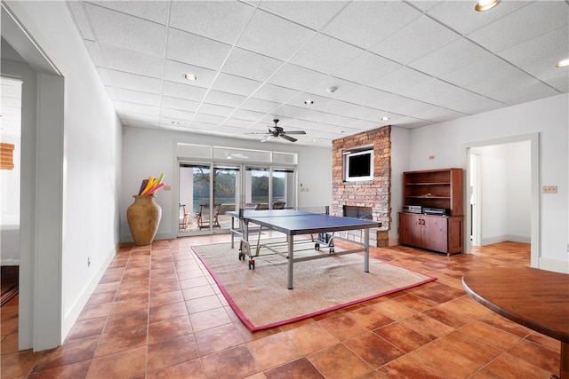 game room with ceiling fan, tile patterned flooring, a stone fireplace, and a drop ceiling