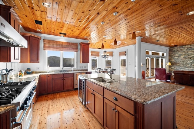 kitchen featuring wood ceiling, stainless steel range, an island with sink, and sink