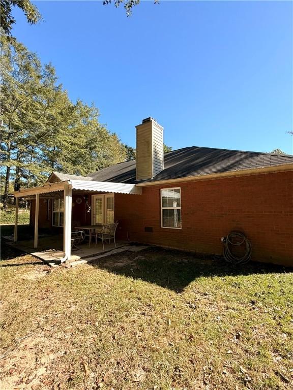 back of house with a patio, a chimney, and a lawn