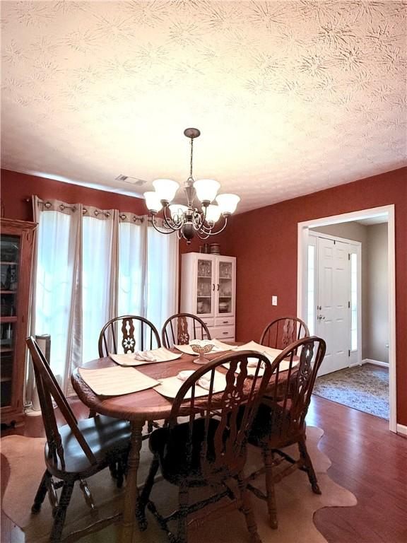 dining room with wood finished floors, a textured ceiling, visible vents, a chandelier, and baseboards
