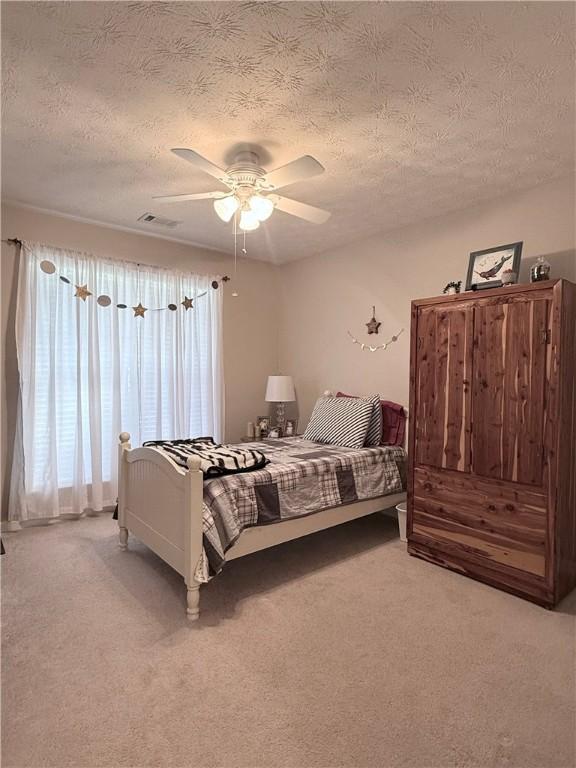 bedroom featuring a textured ceiling, ceiling fan, visible vents, and carpet floors
