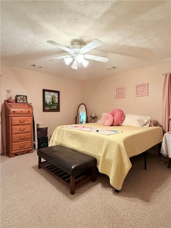 bedroom featuring light colored carpet, a textured ceiling, and ceiling fan