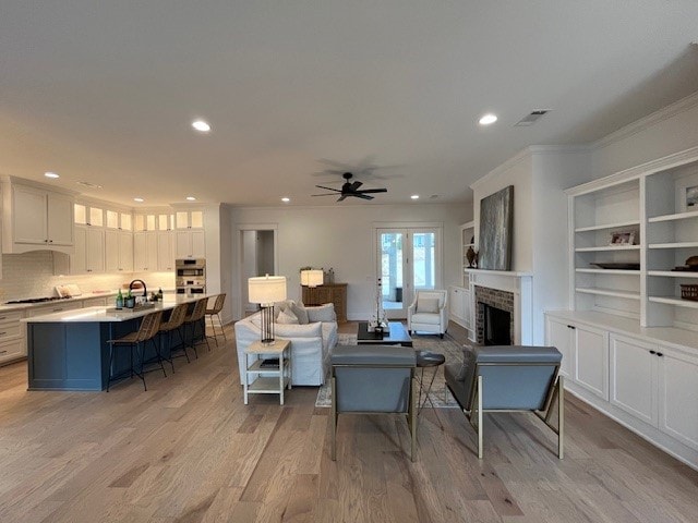 living room featuring a fireplace, sink, ornamental molding, ceiling fan, and light wood-type flooring