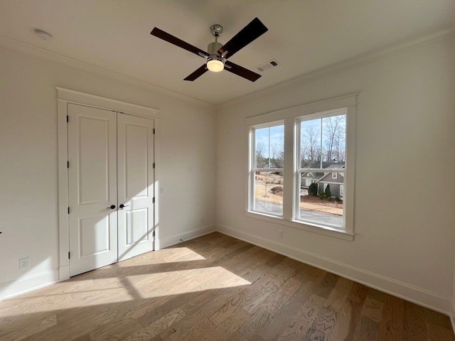 unfurnished bedroom featuring crown molding, ceiling fan, light wood-type flooring, and a closet