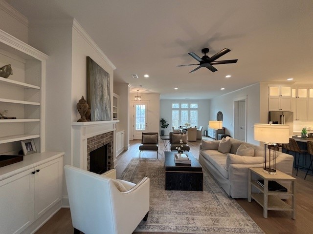 living room featuring a brick fireplace, crown molding, and wood-type flooring