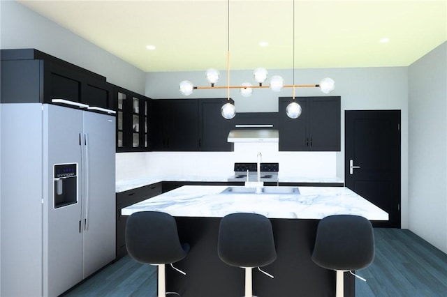 kitchen with white fridge with ice dispenser, sink, hanging light fixtures, light stone counters, and a center island with sink