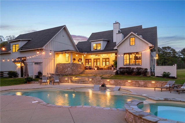 rear view of property with board and batten siding, a shingled roof, a patio, and a chimney