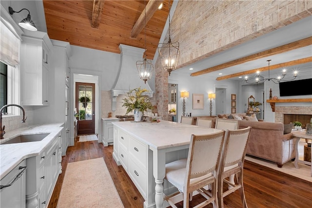 kitchen with light stone countertops, a sink, a notable chandelier, dark wood-style floors, and beam ceiling