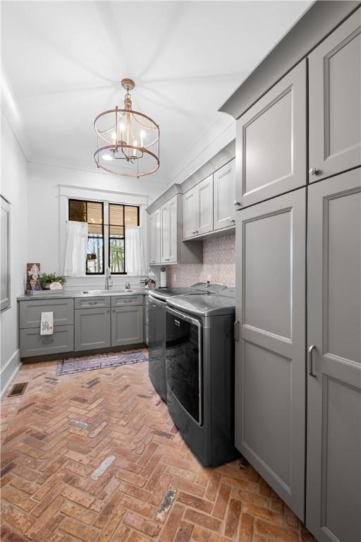 clothes washing area featuring a notable chandelier, visible vents, washer and clothes dryer, cabinet space, and a sink