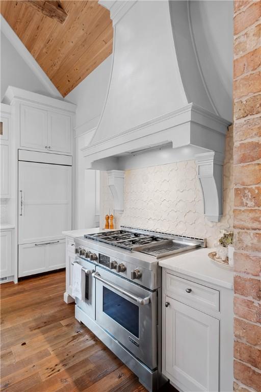kitchen with white cabinetry, custom exhaust hood, lofted ceiling, high quality appliances, and decorative backsplash