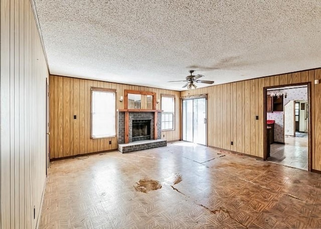 unfurnished living room featuring wood walls, a brick fireplace, ceiling fan, parquet flooring, and a textured ceiling