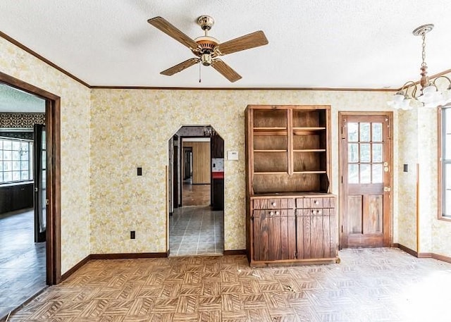 unfurnished living room with a textured ceiling, ceiling fan with notable chandelier, a wealth of natural light, and ornamental molding