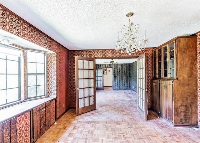 unfurnished dining area featuring ceiling fan with notable chandelier, french doors, light parquet floors, and a textured ceiling