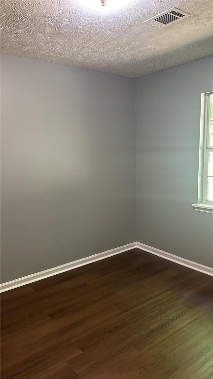 spare room featuring dark wood-type flooring and a textured ceiling