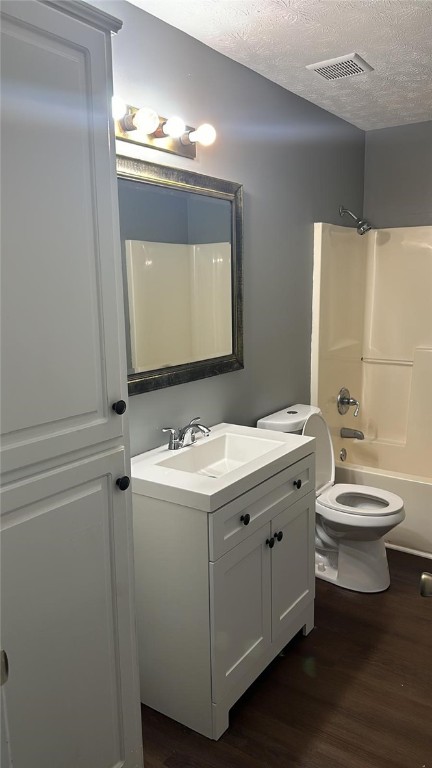 full bathroom with vanity,  shower combination, toilet, a textured ceiling, and wood-type flooring