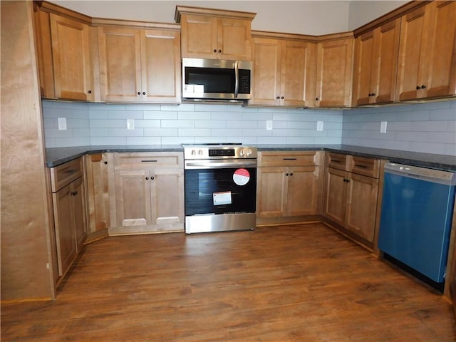 kitchen with stainless steel appliances, tasteful backsplash, dark hardwood / wood-style flooring, and dark stone counters