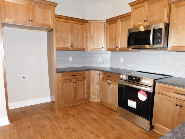 kitchen with tasteful backsplash, wood-type flooring, dark stone counters, and appliances with stainless steel finishes