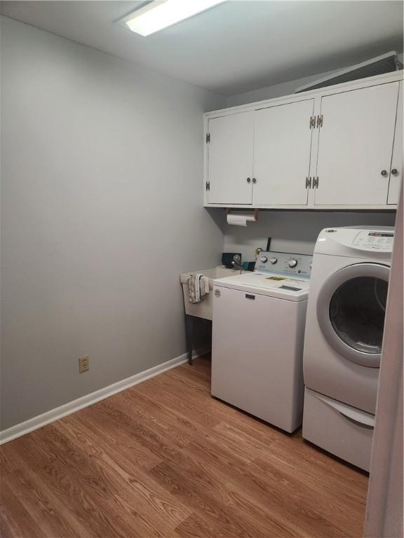 washroom with washing machine and clothes dryer, cabinets, and light hardwood / wood-style floors