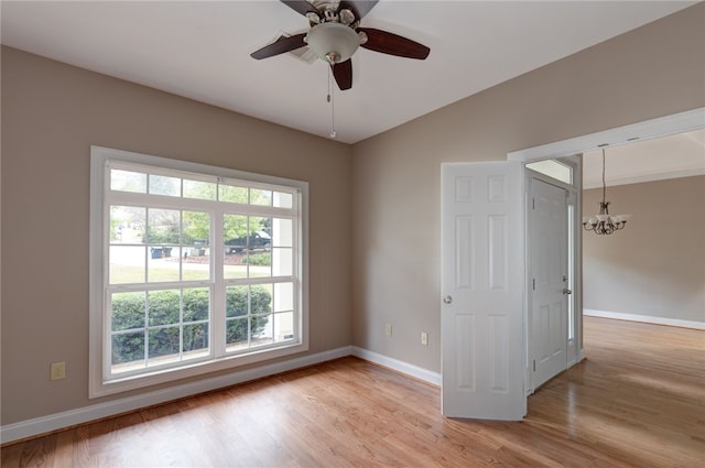 empty room with ceiling fan with notable chandelier and light hardwood / wood-style floors