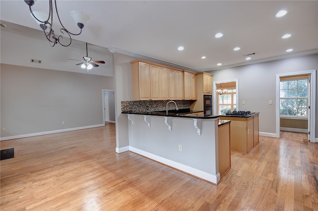 kitchen featuring kitchen peninsula, light wood-type flooring, tasteful backsplash, sink, and decorative light fixtures