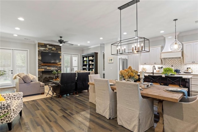 dining space featuring ceiling fan, sink, a stone fireplace, dark hardwood / wood-style flooring, and crown molding