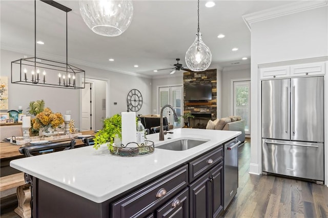 kitchen with stainless steel appliances, ceiling fan, sink, a stone fireplace, and an island with sink