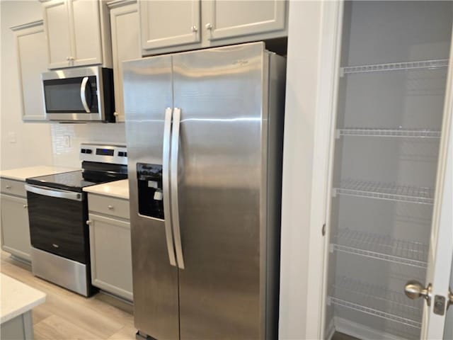 kitchen featuring light countertops, tasteful backsplash, light wood-type flooring, and appliances with stainless steel finishes