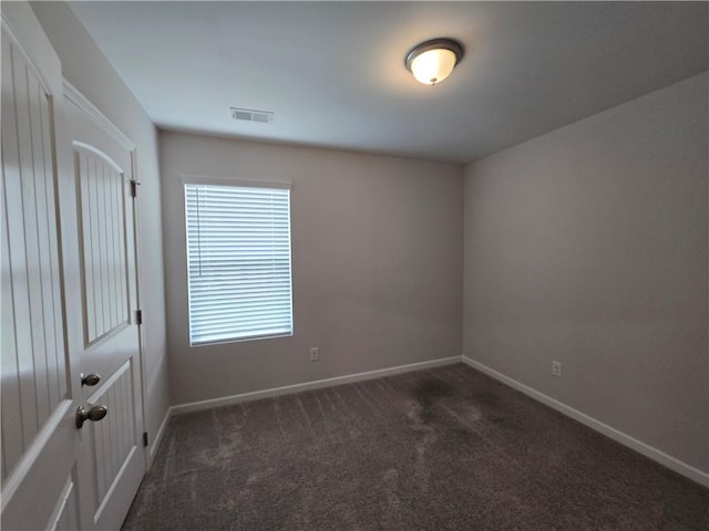 spare room featuring baseboards, visible vents, and dark carpet
